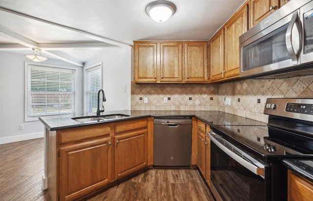 kitchen with a peninsula, dark countertops, stainless steel appliances, and a sink