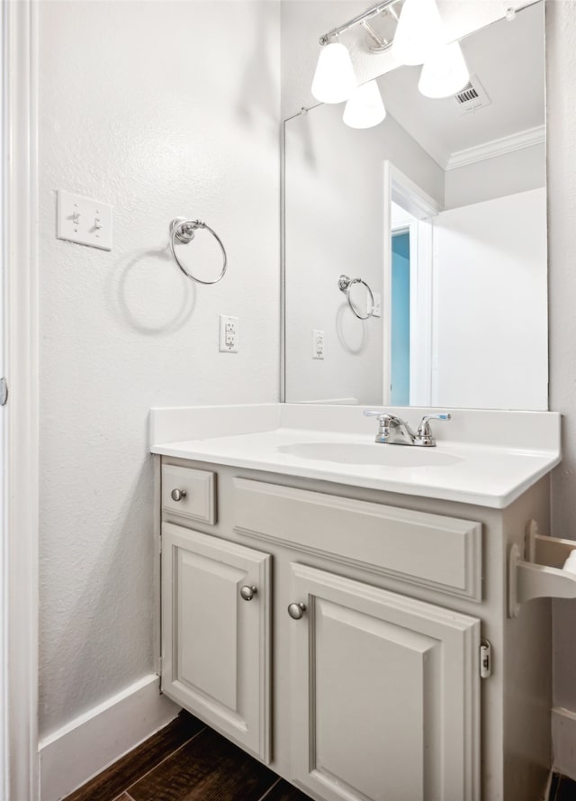 bathroom with wood finished floors, visible vents, baseboards, vanity, and crown molding