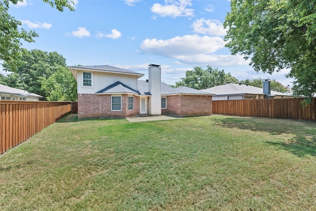 rear view of house featuring a yard, a fenced backyard, brick siding, and a chimney