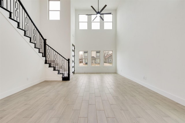 unfurnished living room featuring stairway, ceiling fan, light wood-style flooring, and baseboards