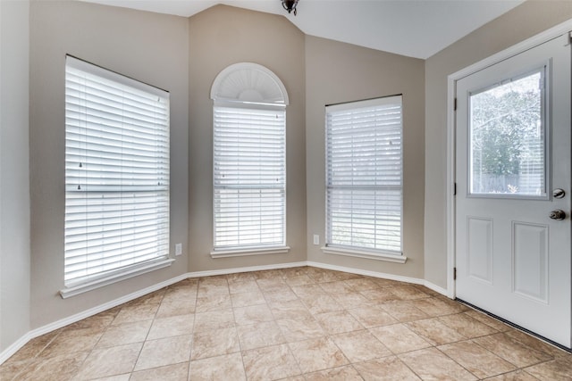 unfurnished dining area with a wealth of natural light, lofted ceiling, light tile patterned flooring, and baseboards