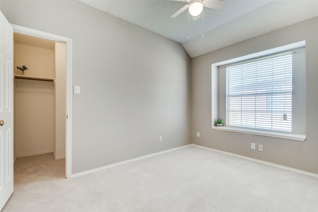 unfurnished bedroom with a walk in closet, a closet, light colored carpet, vaulted ceiling, and baseboards