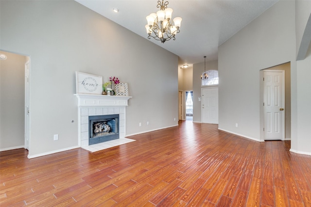 unfurnished living room featuring a chandelier, high vaulted ceiling, a tiled fireplace, and wood finished floors