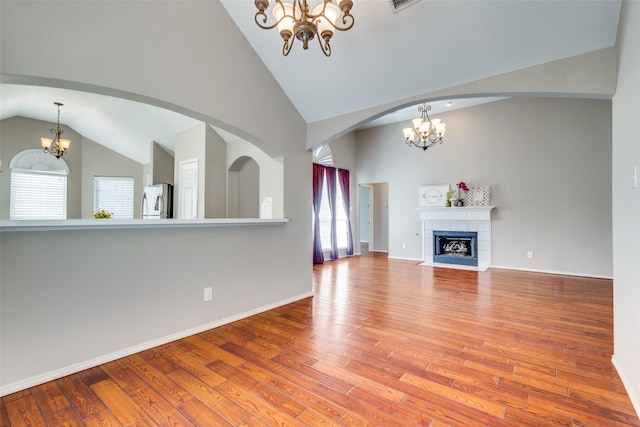 unfurnished living room featuring wood finished floors, baseboards, a tiled fireplace, and an inviting chandelier