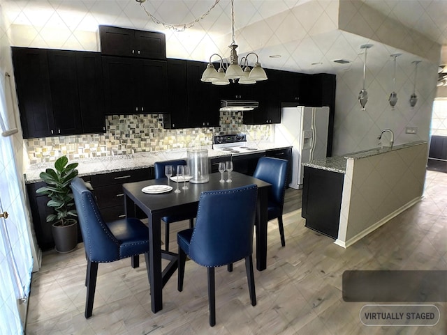 kitchen featuring light stone counters, under cabinet range hood, range with electric cooktop, dark cabinetry, and white fridge with ice dispenser