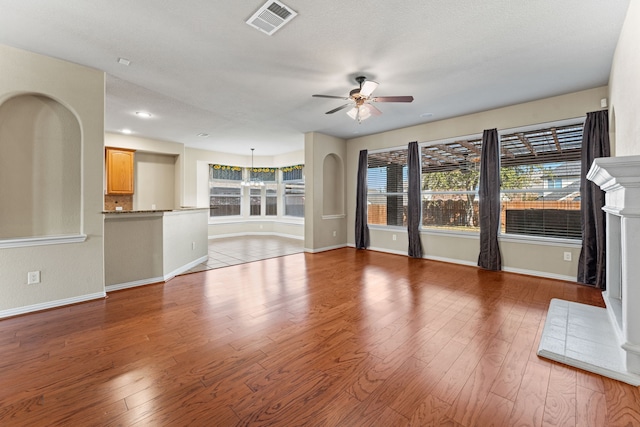 unfurnished living room with a healthy amount of sunlight, light wood-style flooring, visible vents, and ceiling fan with notable chandelier