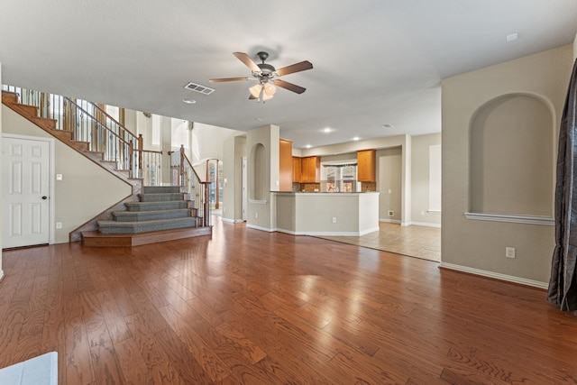 unfurnished living room with ceiling fan, visible vents, baseboards, light wood-style floors, and stairway