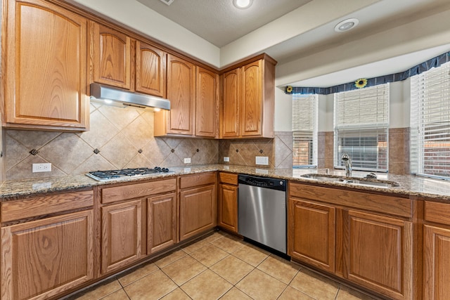 kitchen featuring stainless steel appliances, stone counters, a sink, and under cabinet range hood