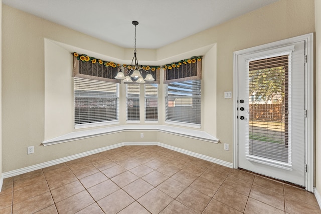 unfurnished dining area featuring baseboards, tile patterned flooring, and an inviting chandelier