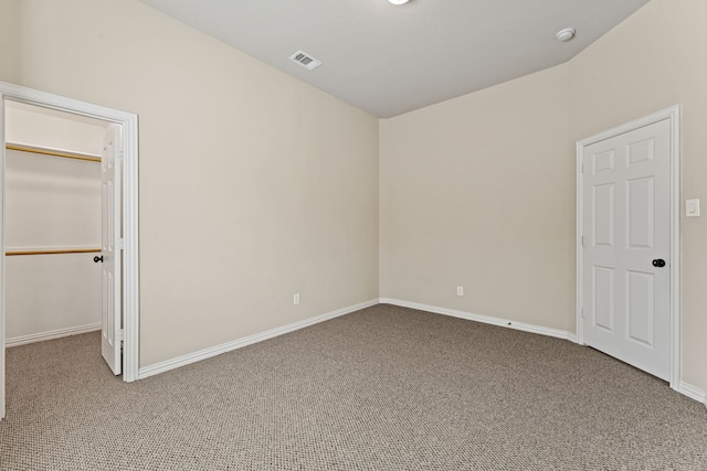 unfurnished bedroom with carpet floors, a walk in closet, visible vents, and baseboards