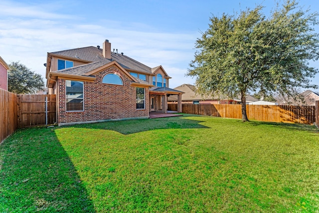 back of house featuring a yard, a fenced backyard, and brick siding