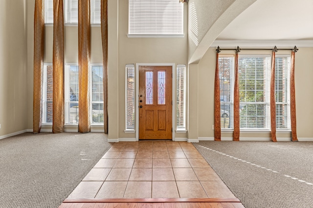 entryway featuring light carpet, light tile patterned floors, baseboards, arched walkways, and a towering ceiling