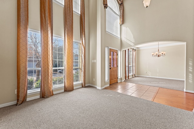 foyer with baseboards, arched walkways, light colored carpet, a towering ceiling, and a notable chandelier