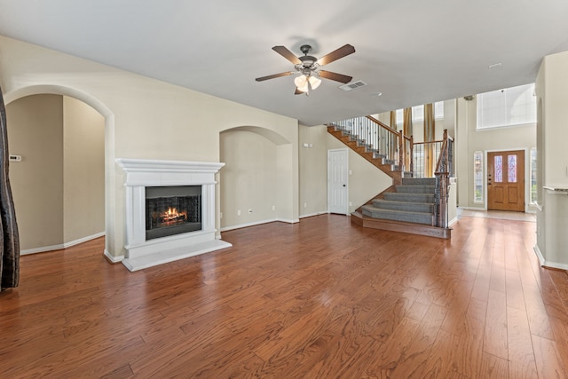 unfurnished living room with a glass covered fireplace, visible vents, stairway, and wood finished floors