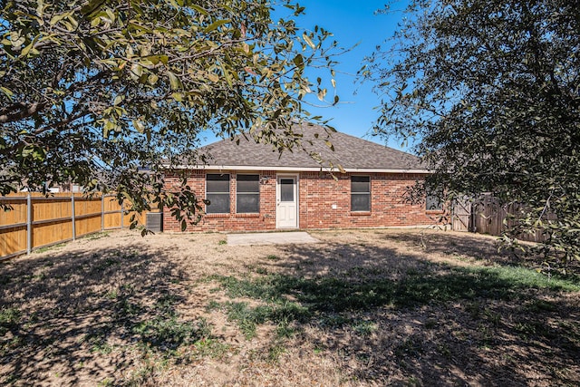 back of house featuring brick siding, roof with shingles, a fenced backyard, and a lawn