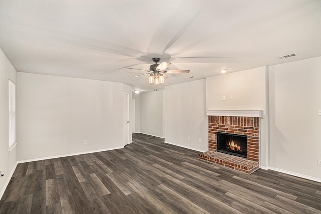 unfurnished living room featuring dark wood-type flooring, visible vents, a ceiling fan, baseboards, and a brick fireplace