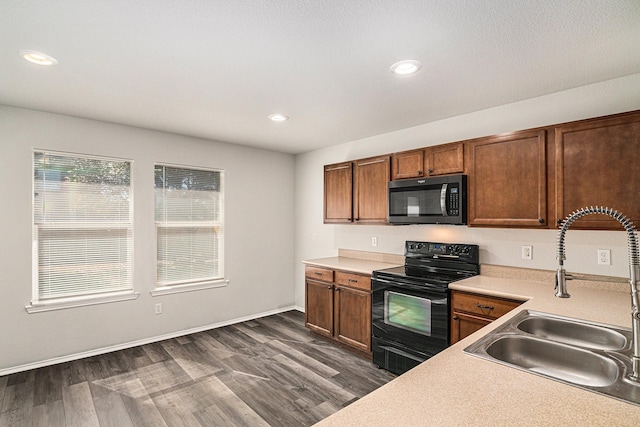 kitchen with light countertops, stainless steel microwave, dark wood-type flooring, a sink, and black / electric stove