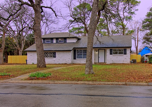 view of front of house featuring a shingled roof, fence, a front lawn, and central AC