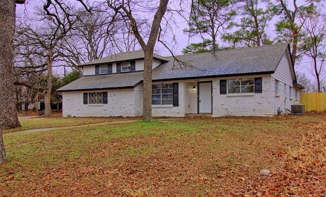 view of front of property with a shingled roof, central AC unit, and a front yard