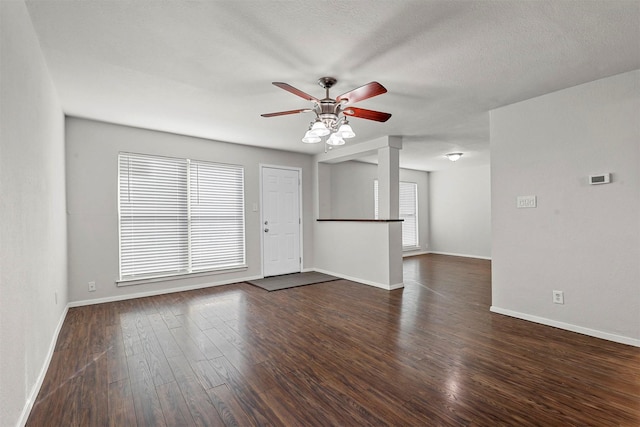 unfurnished room featuring ceiling fan, dark wood finished floors, a wealth of natural light, and baseboards