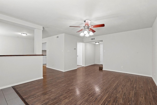 empty room with dark wood-style floors, visible vents, a ceiling fan, and baseboards