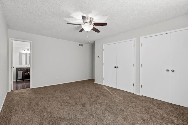 unfurnished bedroom with a textured ceiling, visible vents, multiple closets, carpet, and ensuite bath