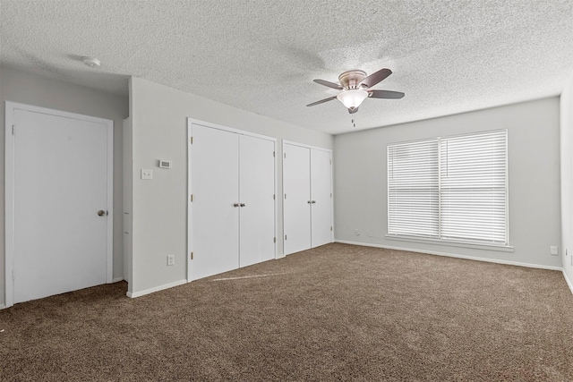 unfurnished bedroom featuring carpet, a textured ceiling, ceiling fan, and multiple closets