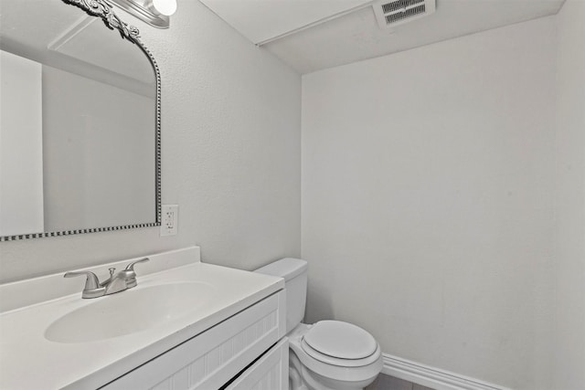 half bath with toilet, vanity, visible vents, and baseboards