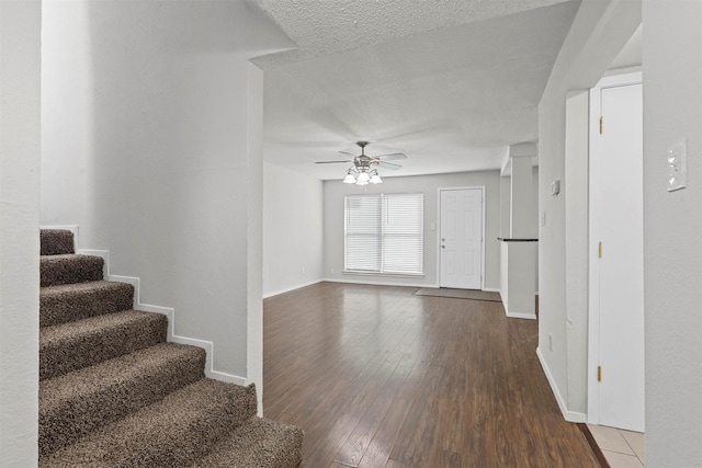 unfurnished living room featuring baseboards, ceiling fan, hardwood / wood-style floors, stairs, and a textured ceiling