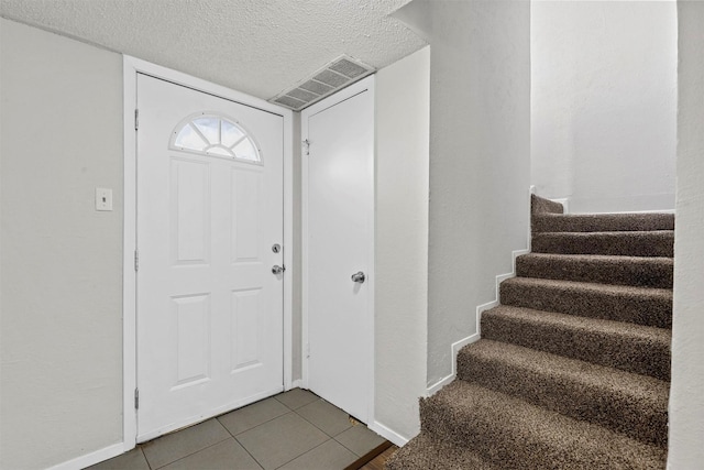 foyer entrance featuring visible vents, a textured ceiling, tile patterned flooring, baseboards, and stairs