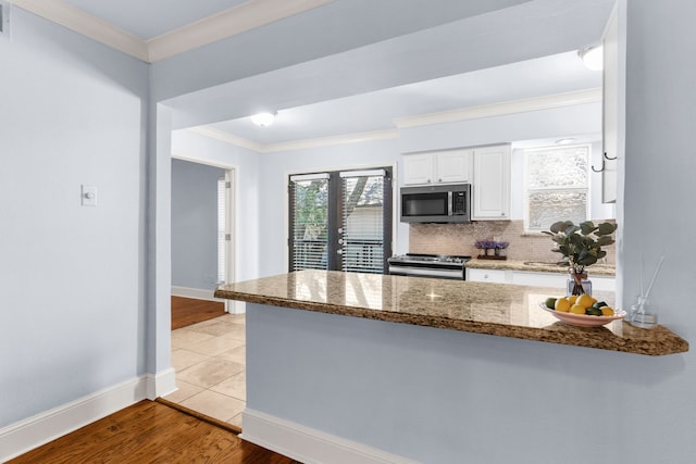 kitchen featuring dark stone counters, stainless steel appliances, white cabinetry, and crown molding