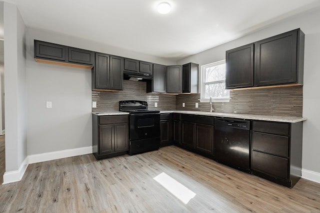 kitchen featuring under cabinet range hood, baseboards, light wood-type flooring, black appliances, and tasteful backsplash