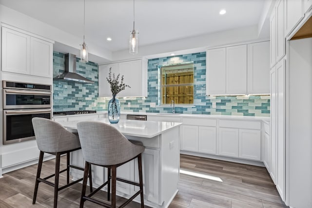 kitchen featuring a kitchen island, white cabinetry, light countertops, appliances with stainless steel finishes, and wall chimney exhaust hood