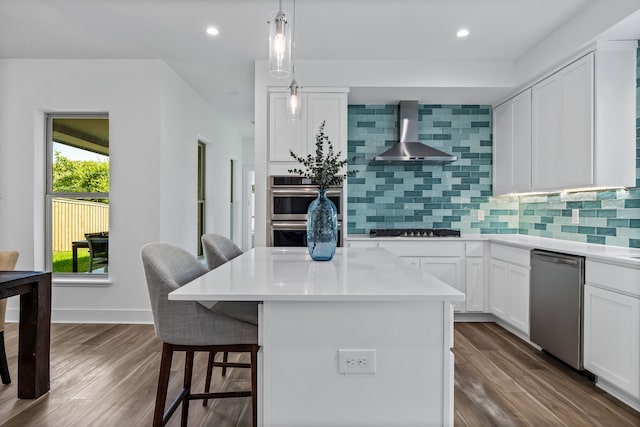 kitchen with stainless steel appliances, white cabinetry, light countertops, wall chimney range hood, and a center island
