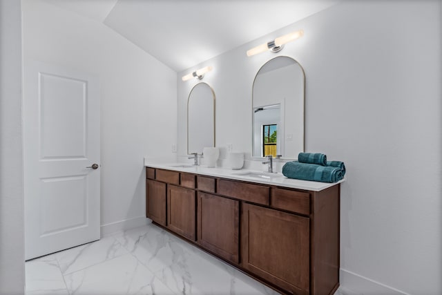 bathroom featuring lofted ceiling, marble finish floor, double vanity, and a sink
