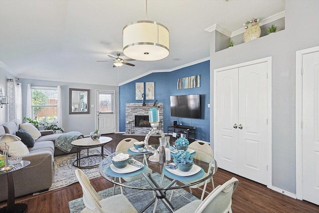 dining space featuring crown molding, a ceiling fan, dark wood-type flooring, and a stone fireplace