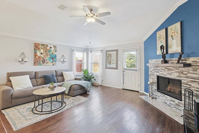 living area featuring dark wood-style floors, visible vents, ornamental molding, ceiling fan, and a stone fireplace