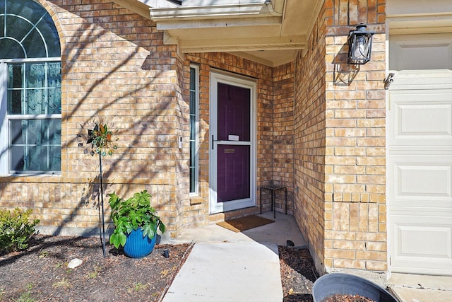 view of exterior entry with a garage and brick siding