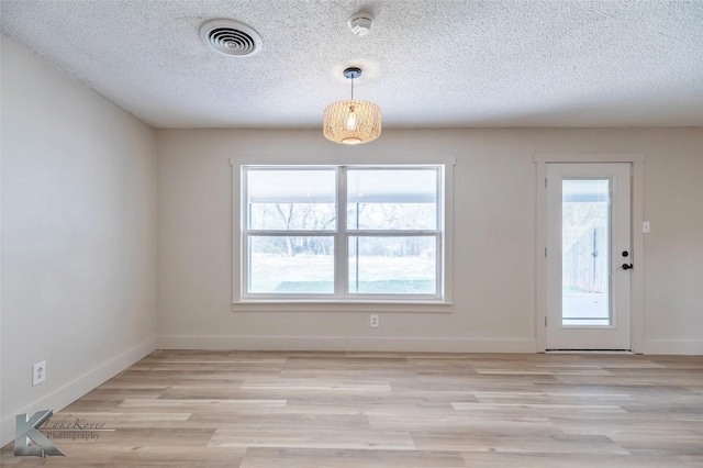 interior space featuring light wood finished floors, baseboards, visible vents, and a textured ceiling