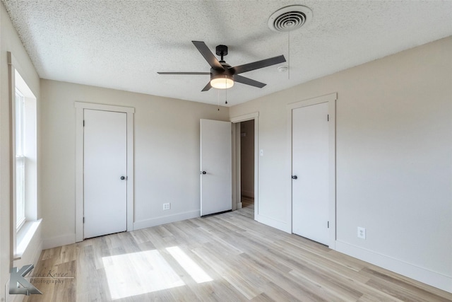 unfurnished bedroom featuring light wood-type flooring, visible vents, a textured ceiling, and baseboards