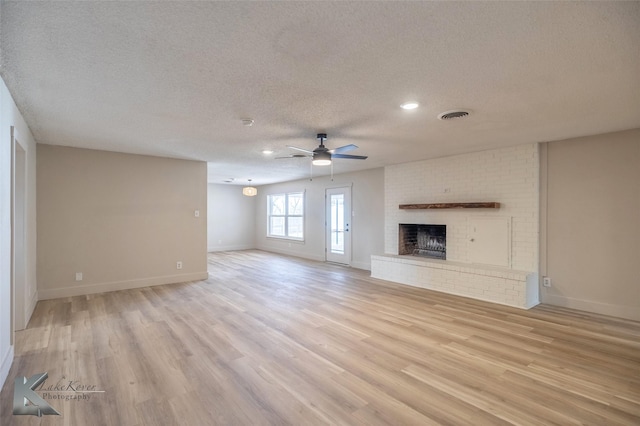 unfurnished living room with visible vents, light wood-style flooring, a brick fireplace, ceiling fan, and a textured ceiling