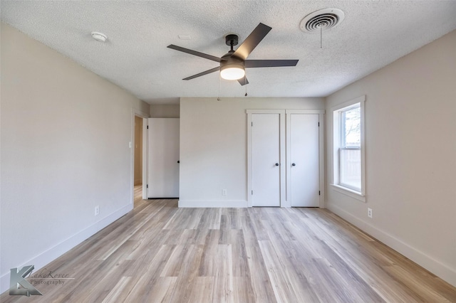 unfurnished bedroom with visible vents, light wood-style flooring, baseboards, and a textured ceiling