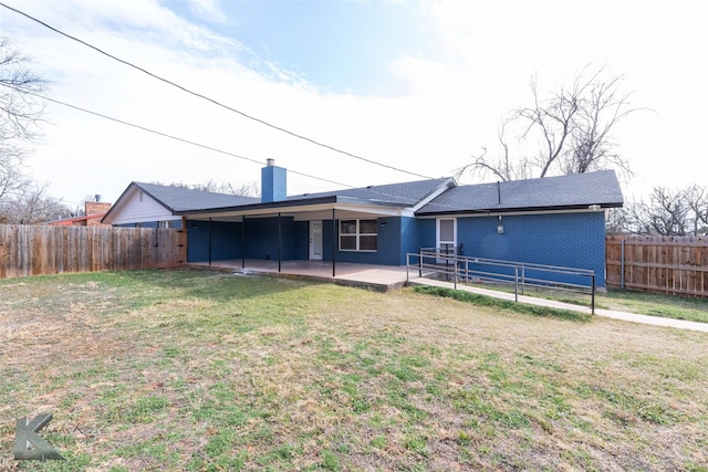 back of property featuring a fenced backyard, a chimney, a yard, a patio area, and brick siding