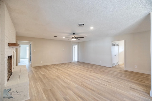 unfurnished living room featuring a textured ceiling, a brick fireplace, visible vents, and light wood-style floors