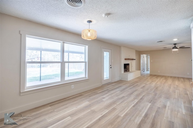 unfurnished living room with light wood finished floors, visible vents, a fireplace with raised hearth, and a textured ceiling