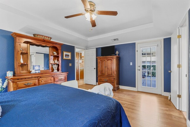 bedroom with visible vents, light wood-style flooring, a ceiling fan, access to outside, and a raised ceiling