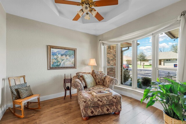 sitting room featuring baseboards, a raised ceiling, hardwood / wood-style floors, and a ceiling fan