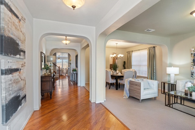 entryway with arched walkways, wood finished floors, visible vents, stairs, and an inviting chandelier