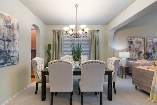 dining space featuring baseboards, arched walkways, a notable chandelier, and light colored carpet