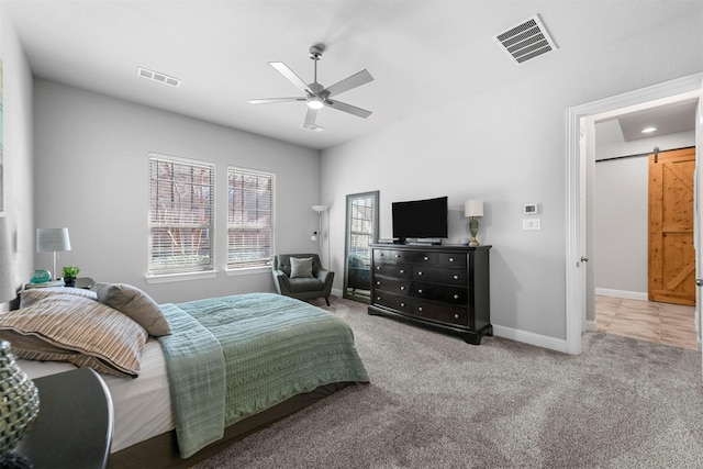 carpeted bedroom featuring a barn door, a ceiling fan, visible vents, and baseboards